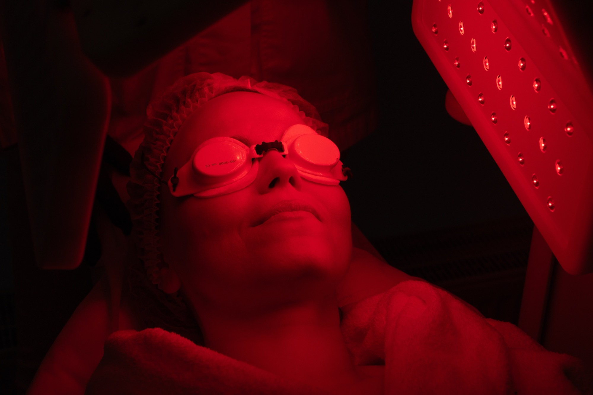 A client bathed in deep red therapy light wearing protective eyewear